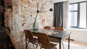 Un salón de conferencias con pared de ladrillo, un ventanal con cortinas y un jarrón con flores sobre la mesa.