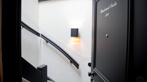 Un interior moderno con una escalera, una luz empotrada en la pared y una puerta que indica “Roosstraat Suite 304”.
