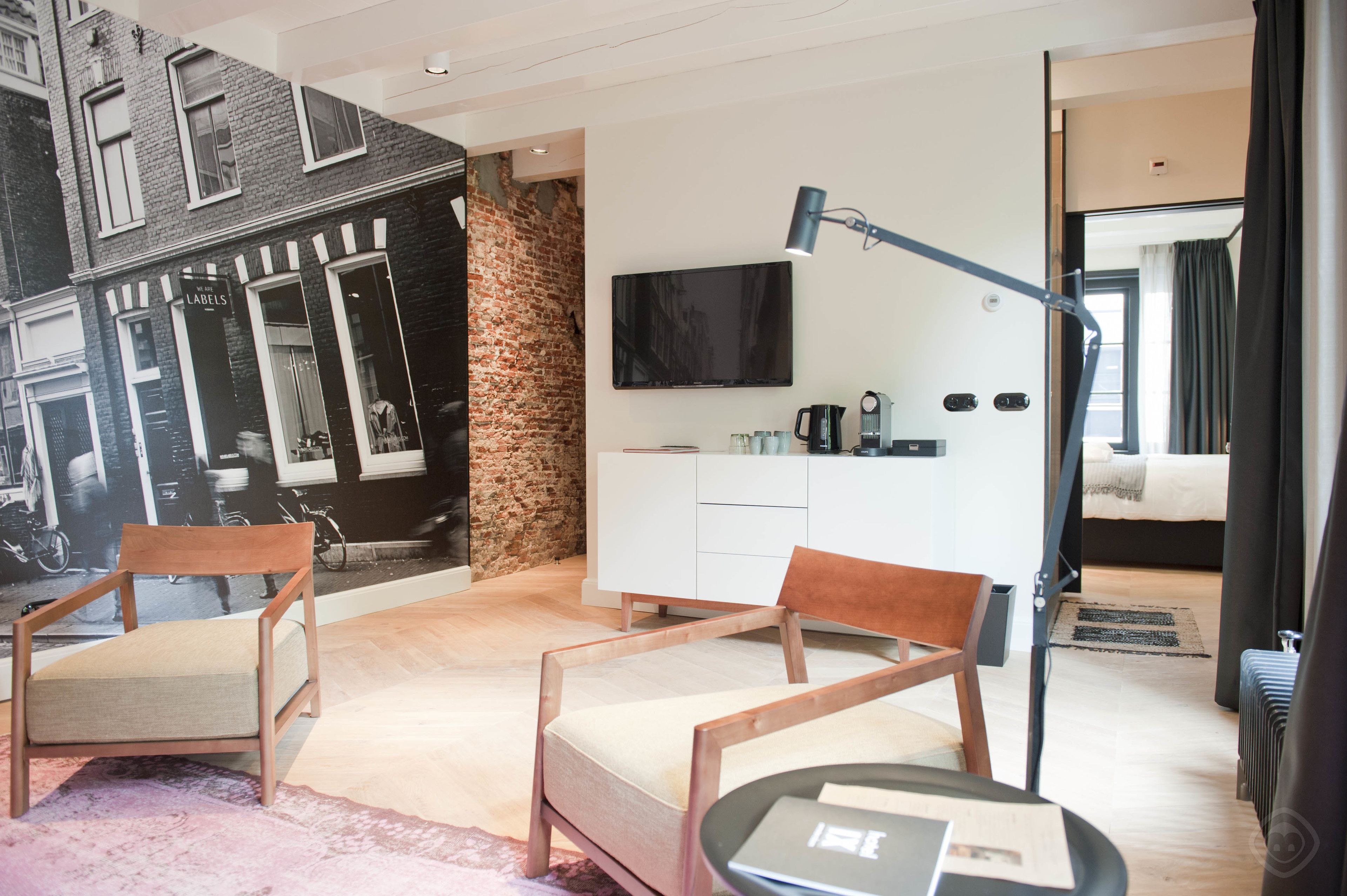 Ein modernes Hotelzimmer mit Backstein-Wandgemälde, einem Flachbildfernseher, einem Bett, einem Schreibtisch mit Stuhl und einem Sofa.