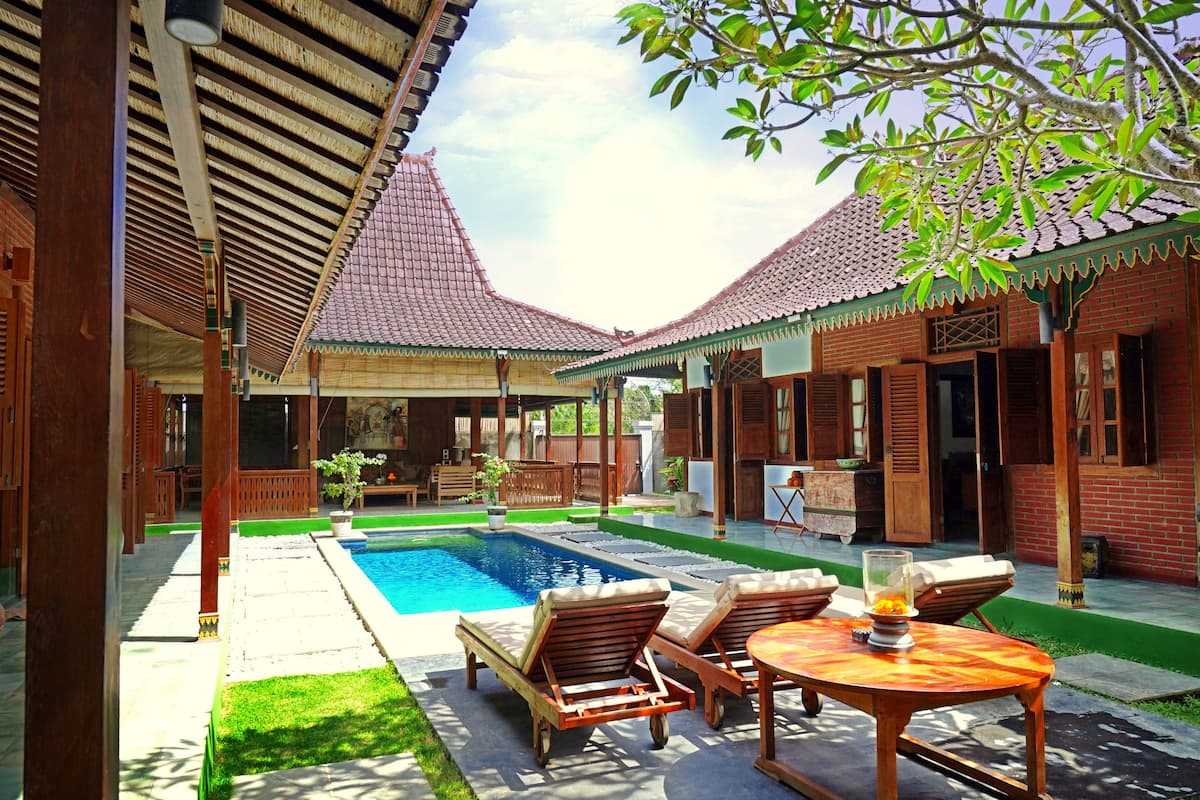 A traditional courtyard with a swimming pool, wooden furniture, and a tiled roof.