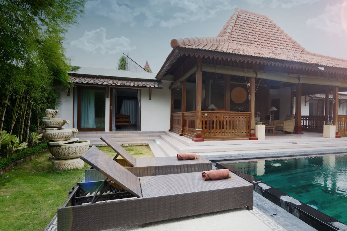 A traditional house with a swimming pool, a covered patio, and a garden with stone planters.