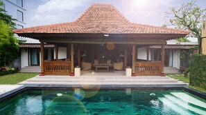 A traditional house with a tiled roof, a covered porch with seating, and a swimming pool in front. - Villa Berawa (Canggu)