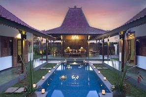 A traditional-style pool with a tiled roof, surrounded by a patio area with seating and candles. - Villa Berawa (Canggu)