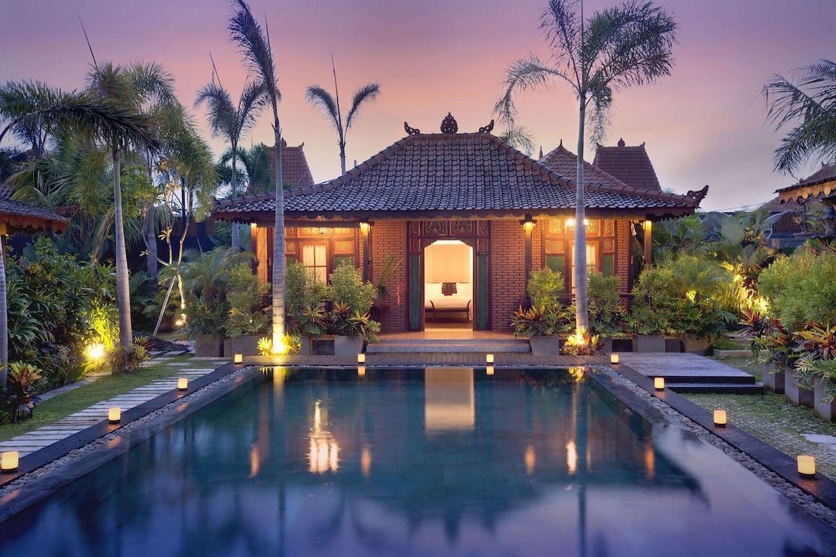 A traditional-style building with a tiled roof, surrounded by a swimming pool and palm trees.
