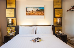 A hotel room with a large bed, white linens, a framed landscape painting, two bedside lamps, a nightstand with a phone, and a vase of flowers.