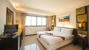 A hotel room with a bed, a TV on a desk, a window with curtains, and a painting on the wall. - Crystal Inn Phuket (Phuket)