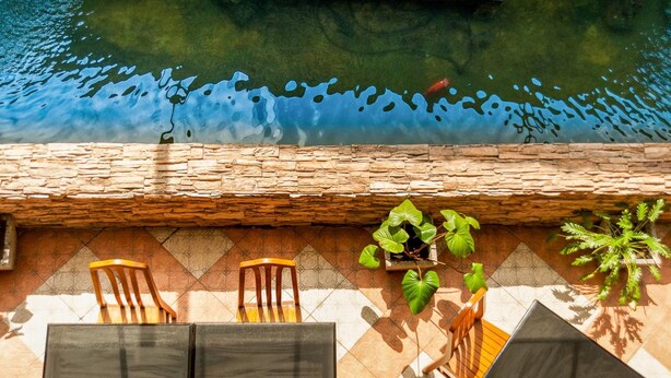 A patio with two wooden chairs and a table, a stone wall, and potted plants. - Crystal Inn Phuket (Phuket)