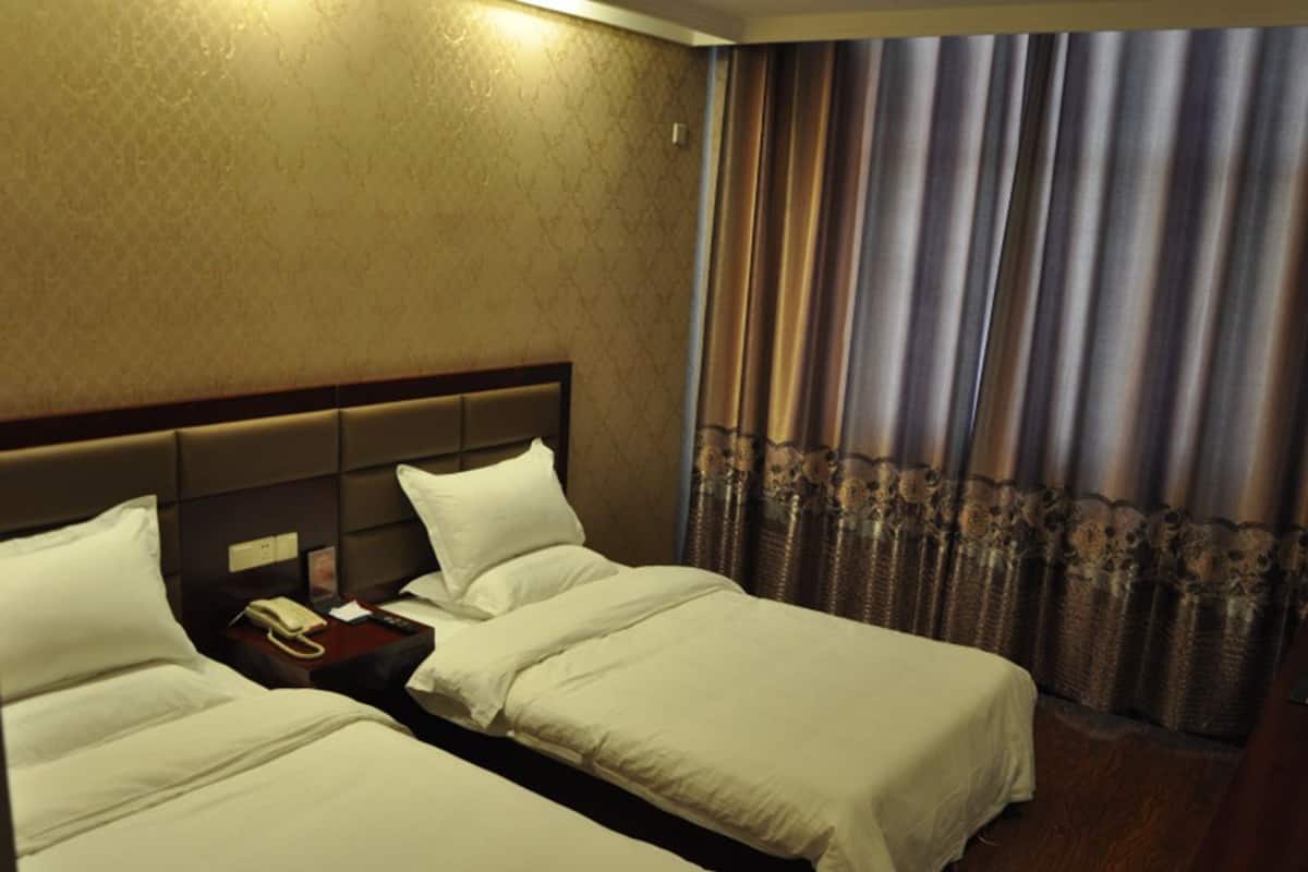 Une chambre d’hôtel avec deux lits simples, une table de chevet avec un téléphone et un rideau orné d’un motif décoratif.