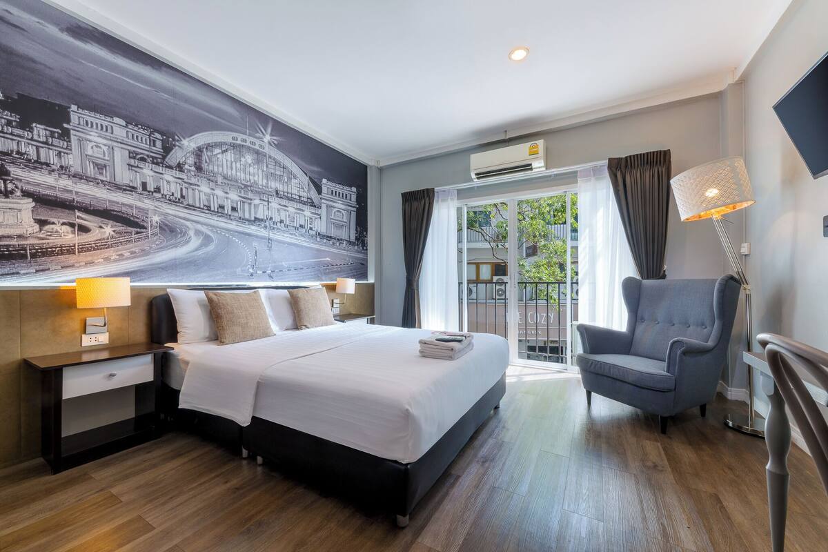 Quarto de hotel com uma cama grande, uma cadeira, uma escrivaninha e uma televisão fixada na parede.