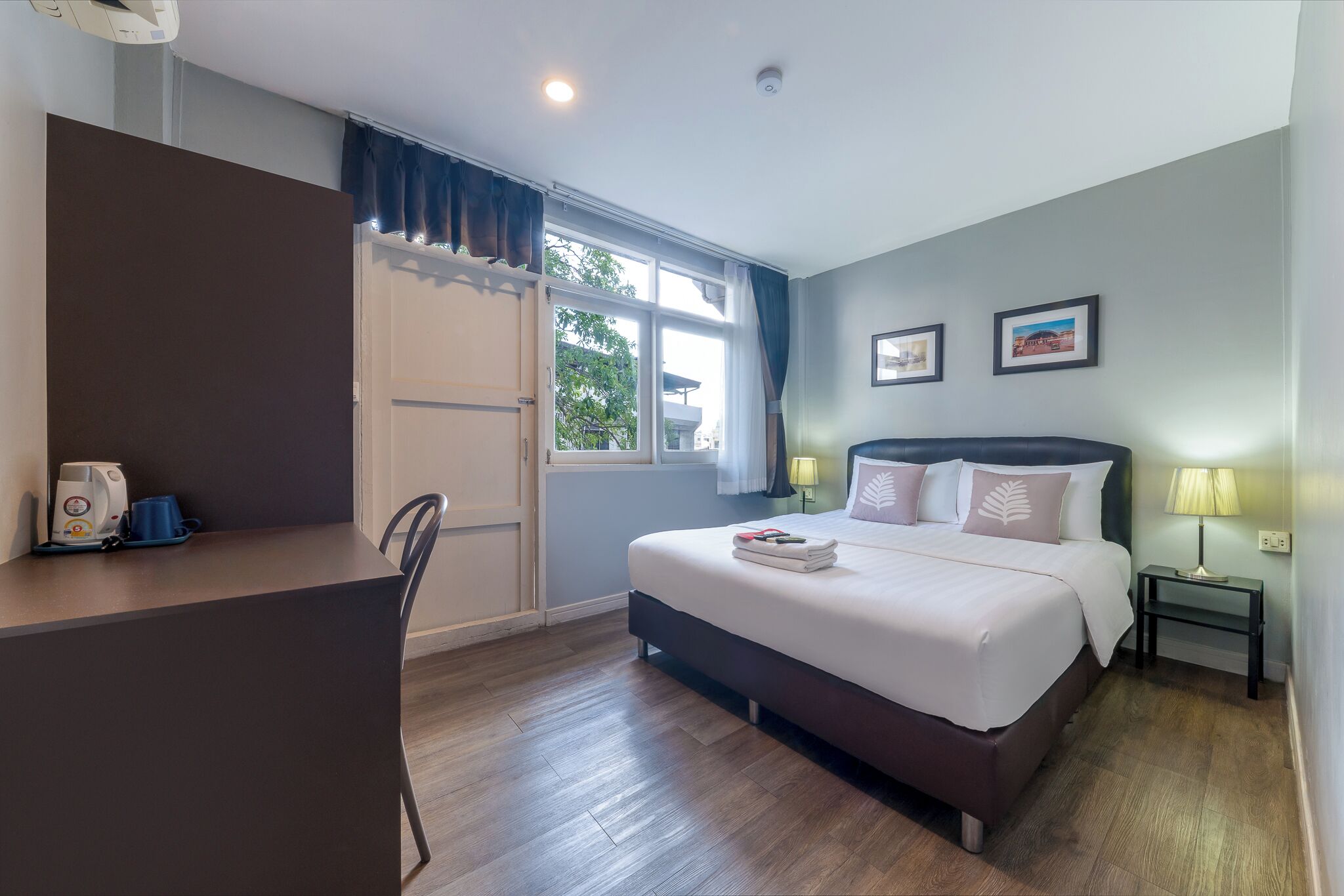 Habitación de hotel con cama, mesita de noche, silla, escritorio y ventana con cortinas.