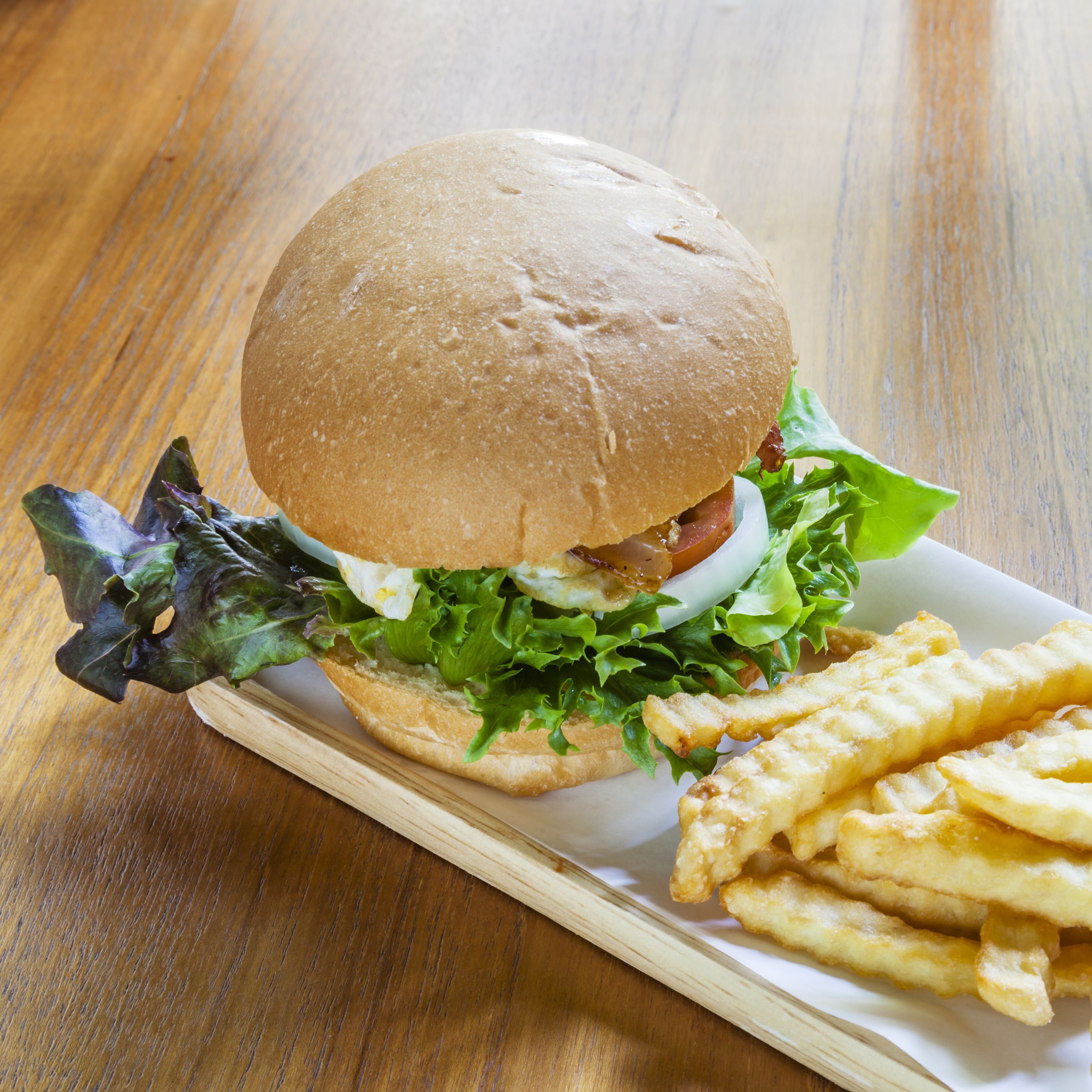 Un sándwich con lechuga y una porción de papas fritas sobre una mesa de madera.