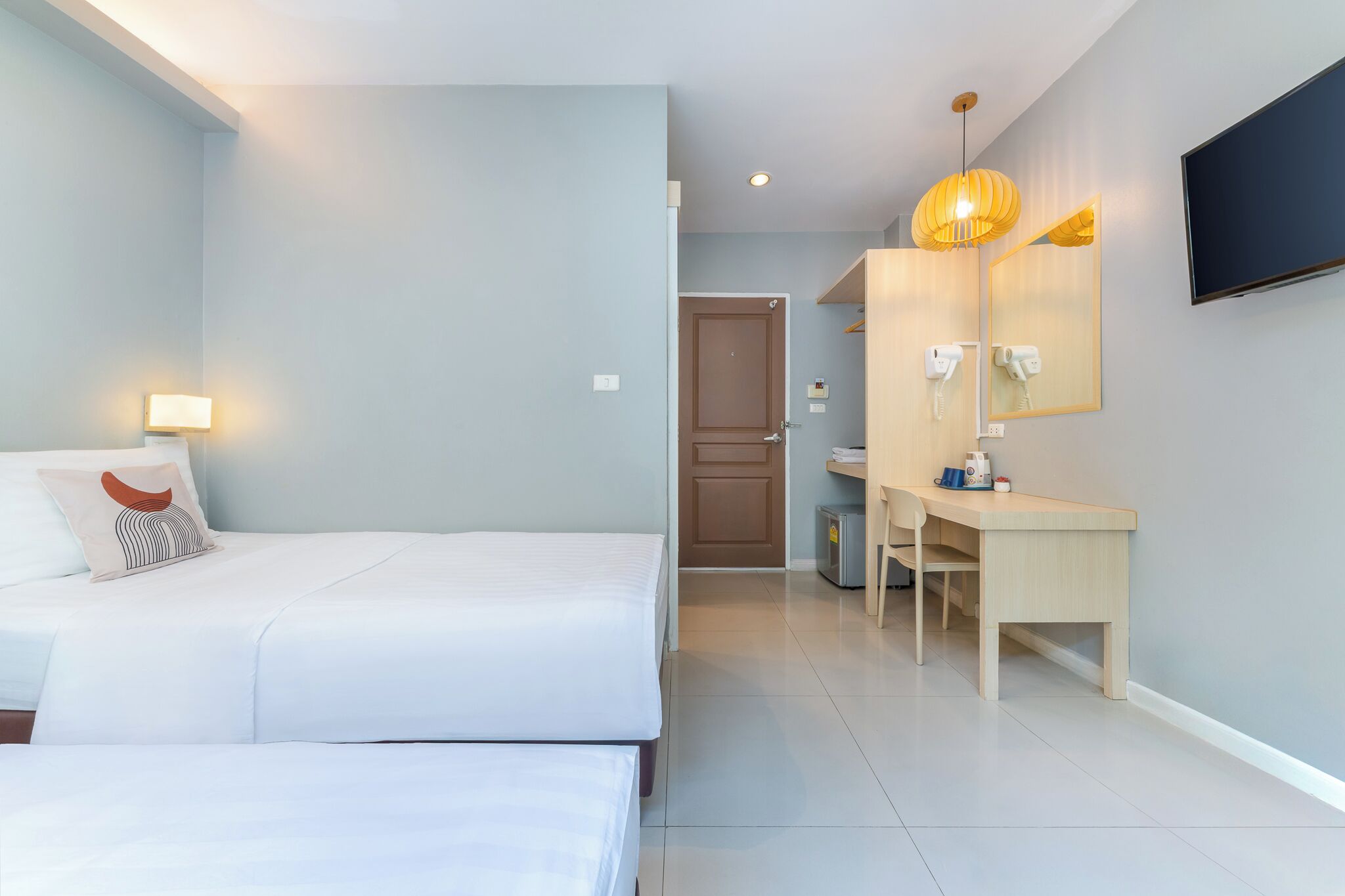 A hotel room with a bed, bedside table, lamp, and a desk with a chair.