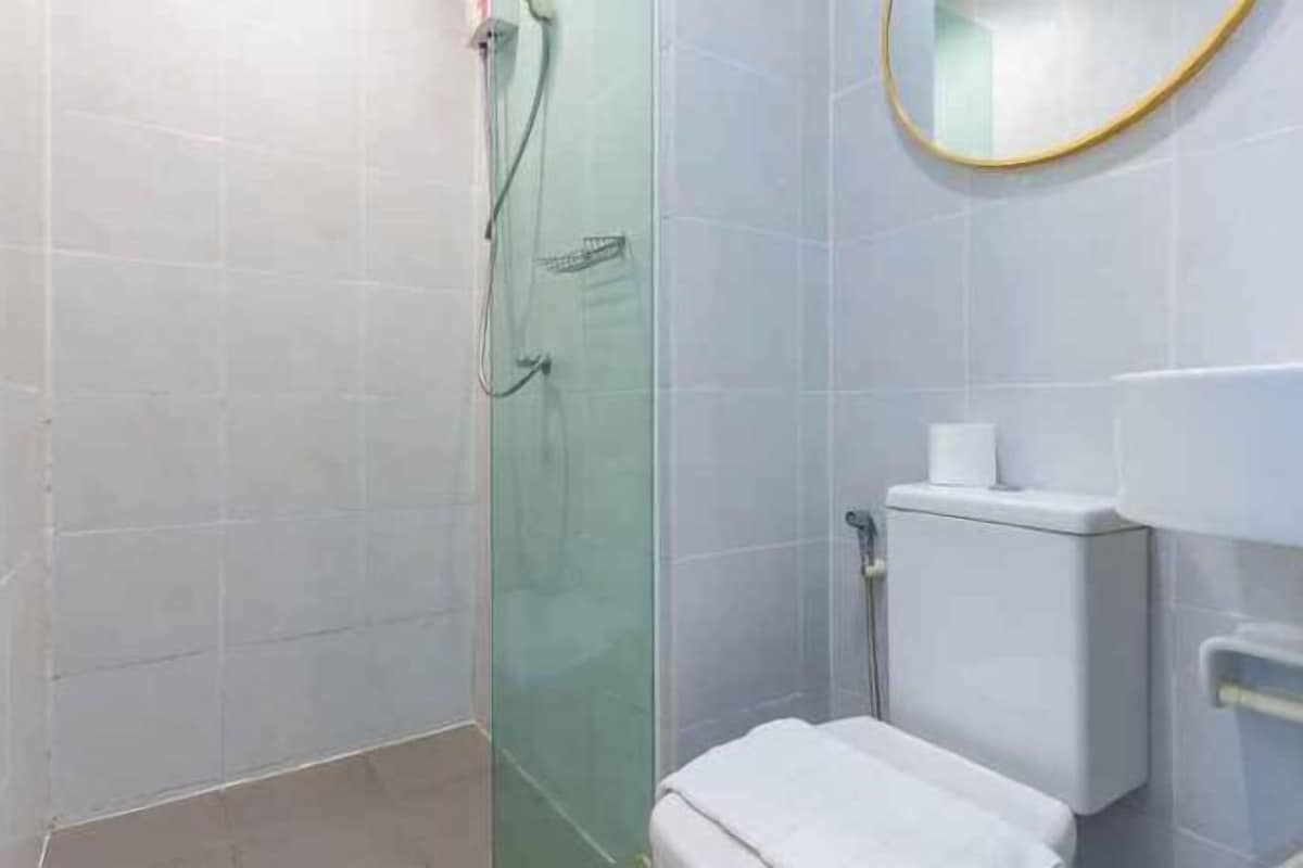 A bathroom with a glass shower enclosure, a toilet, and a mirror with a gold frame.