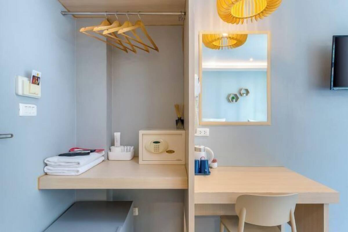 Quarto moderno com escrivaninha, cadeira, cabideiro e prateleira pequena com artigos de higiene pessoal.