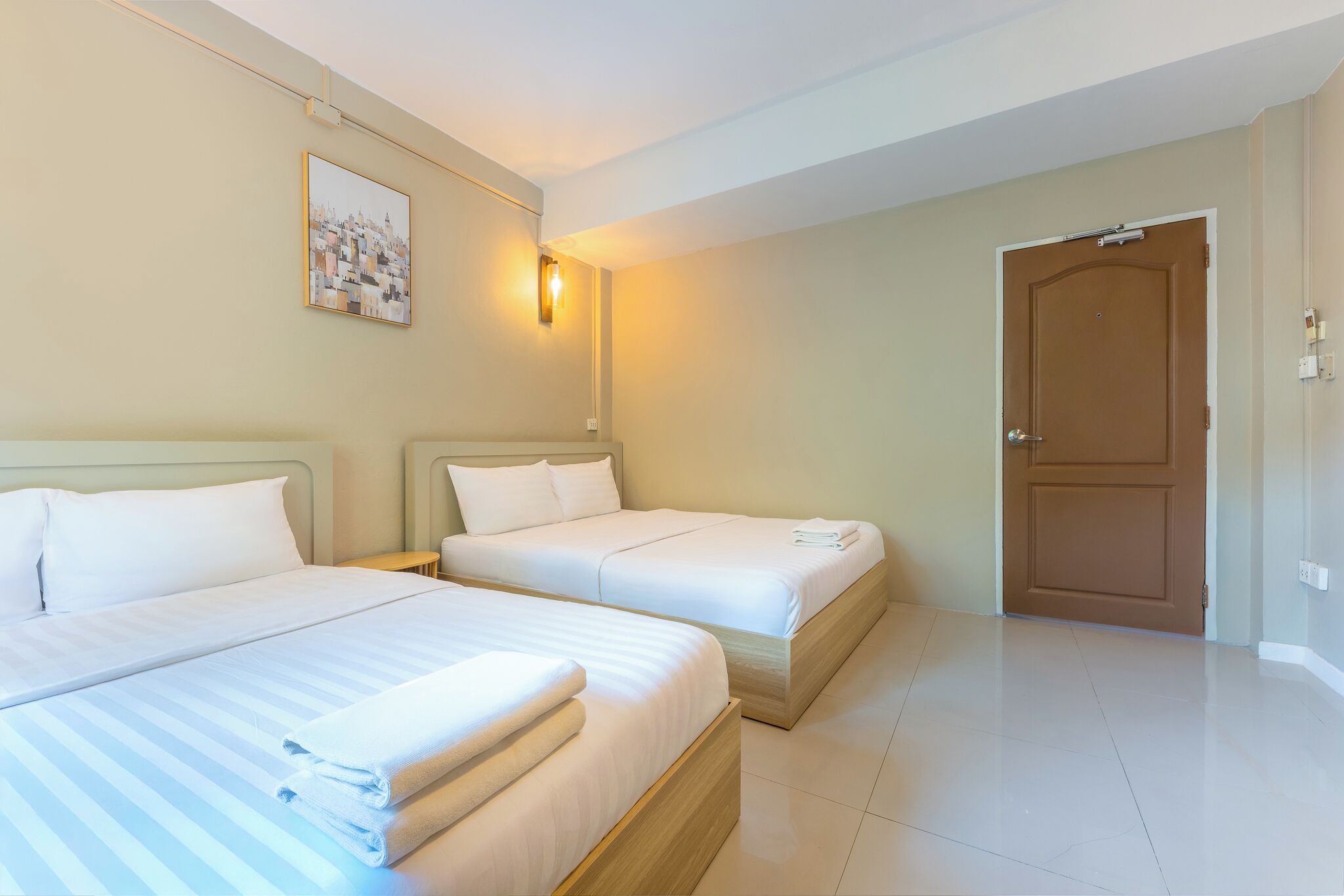 A hotel room with two beds, a door, and a wall-mounted light fixture.