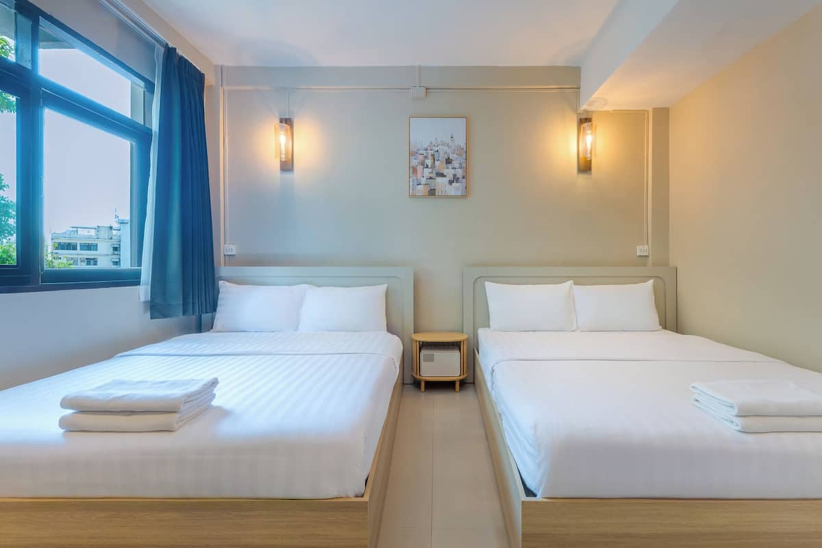 Quarto de hotel com duas camas de solteiro, uma pequena mesa de cabeceira, uma luminária na parede e uma pintura com vista para a cidade.