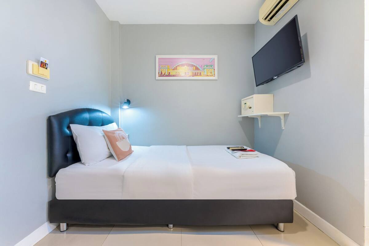 Quarto moderno com cama, televisão fixada na parede, mesa de cabeceira e quadro emoldurado.