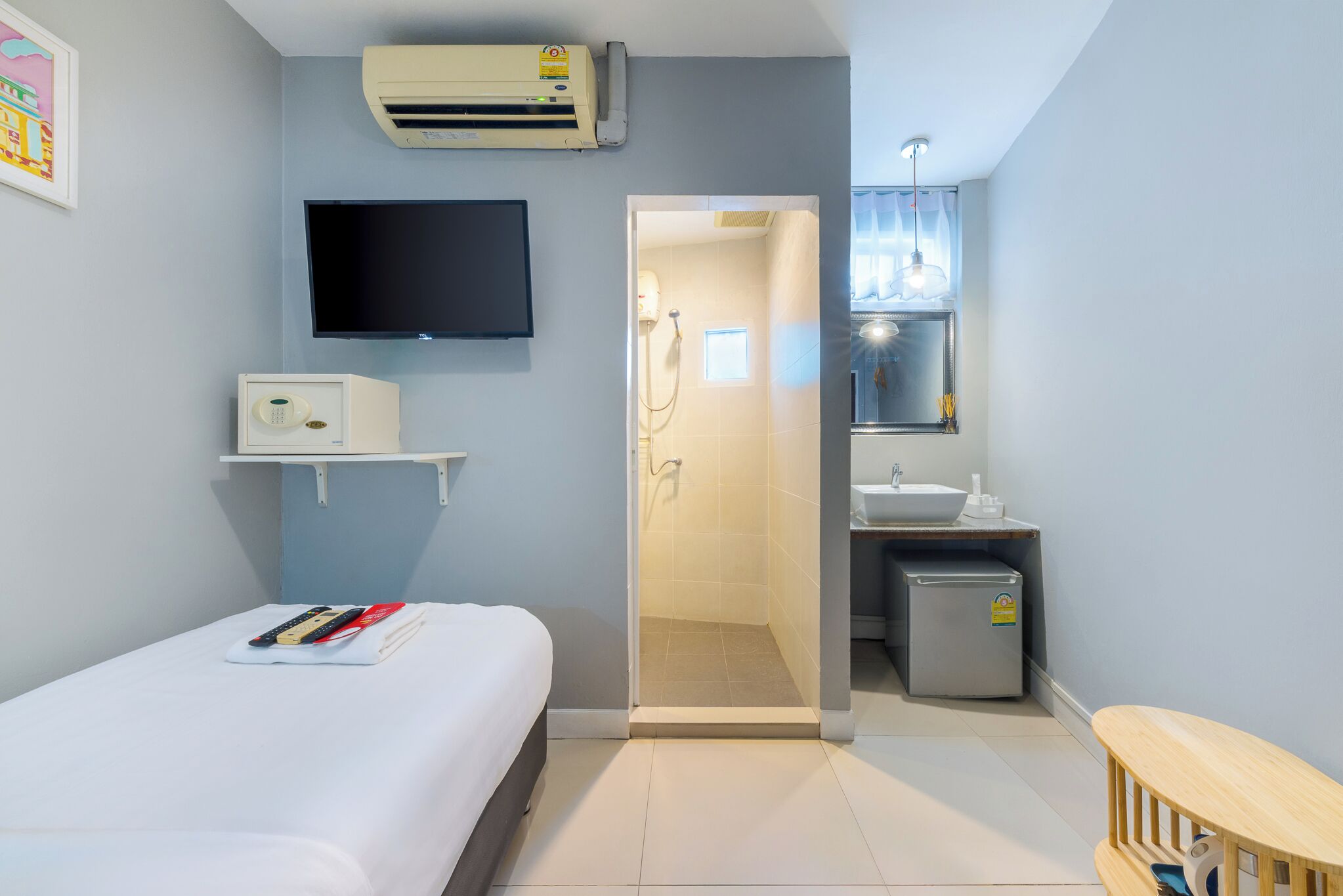 Hotelkamer met een bed, een televisie, een airconditioning, een kleine koelkast en een badkamer met douche en wastafel.