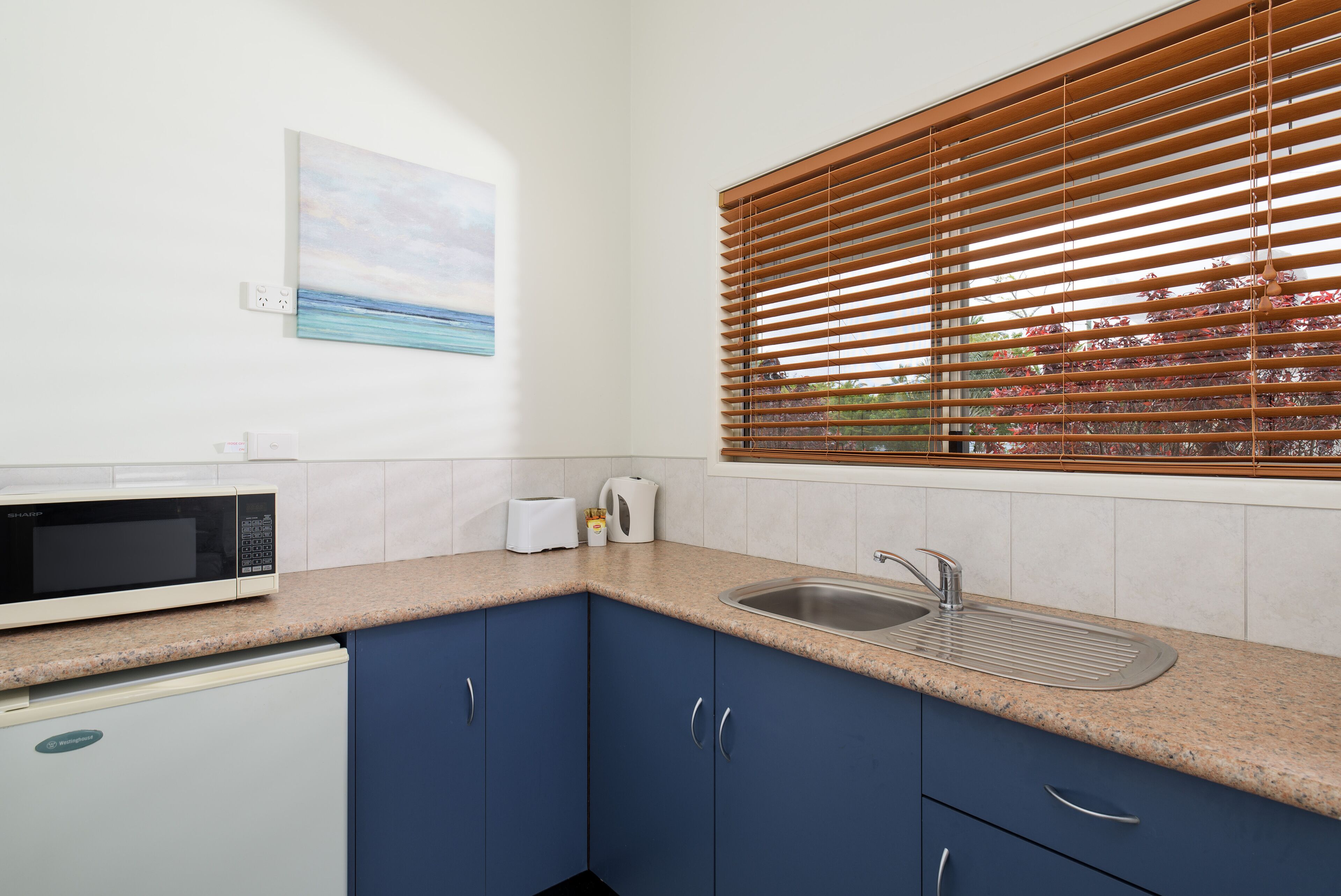 A kitchen with a microwave, toaster, sink, and blue cabinets.