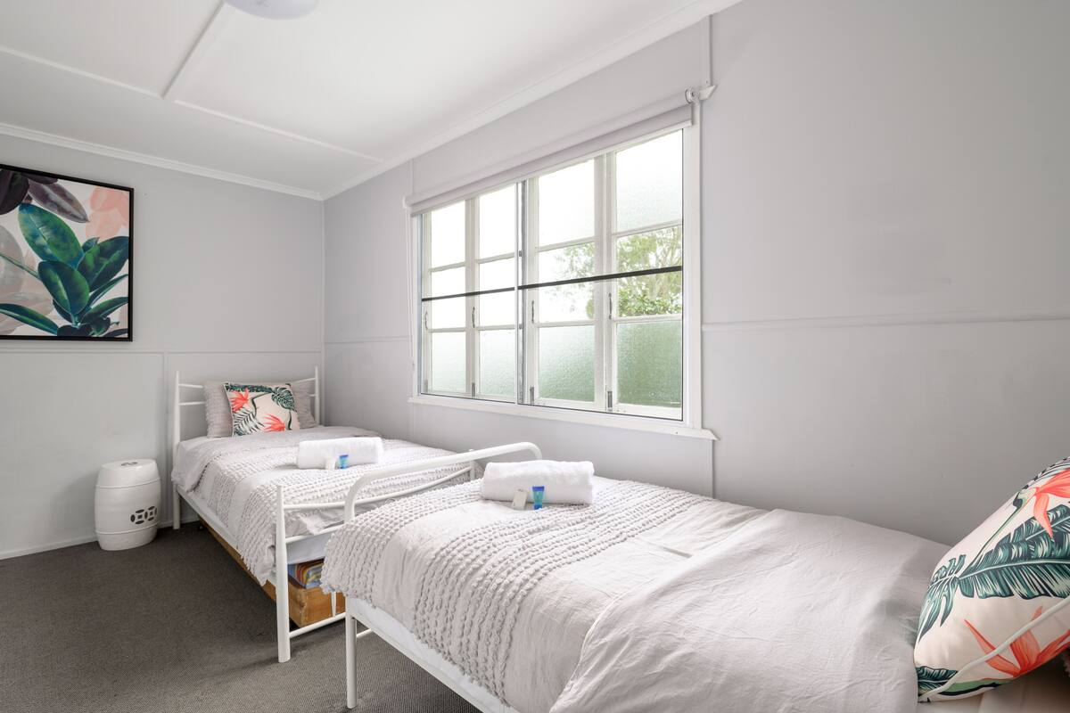Une petite chambre propre, avec deux lits simples, une fenêtre et une poubelle.