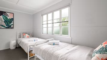 Quarto pequeno e limpo com duas camas de solteiro, uma janela e uma lixeira.
