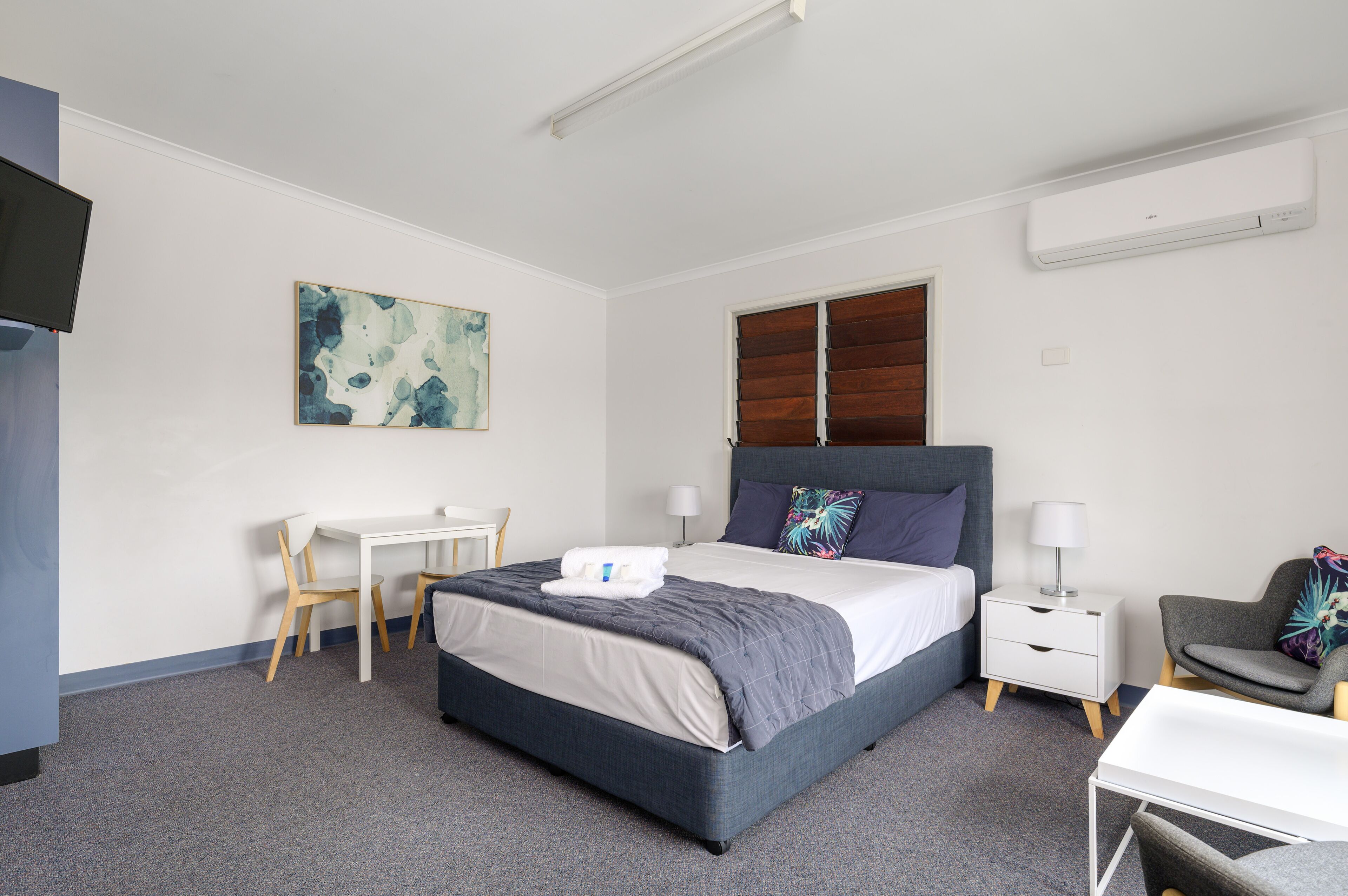 Une chambre d’hôtel équipée d’un lit, d’un bureau, d’une chaise, d’une table de chevet et d’un téléviseur fixé au mur.