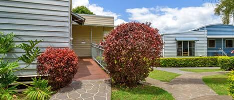 A residential building with a stone pathway leading to a covered entrance, surrounded by well-maintained hedges and a lawn.