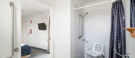 Un baño de hotel con ducha, lavamanos y una cama en la habitación contigua.