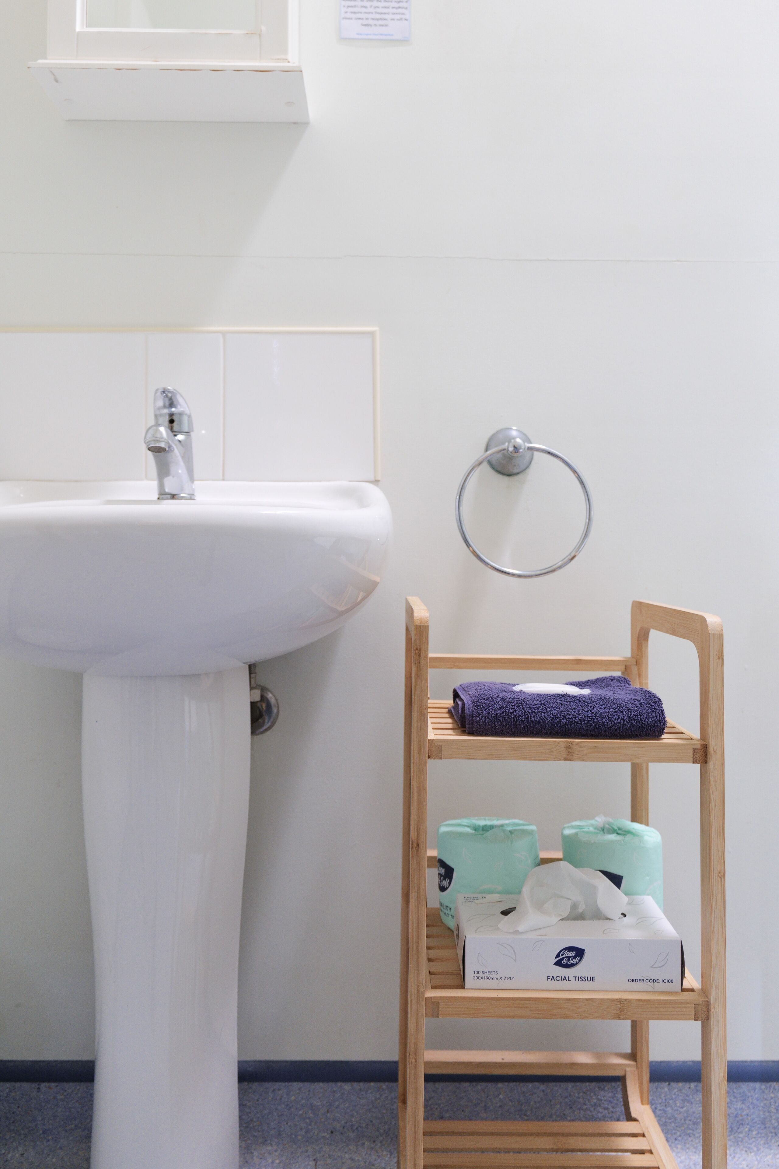 A bathroom with a white sink, a wooden shelf with a folded towel, and a box of facial tissue.