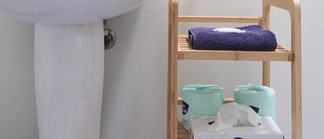 A bathroom with a white sink, a wooden shelf with a folded towel, and a box of facial tissue.