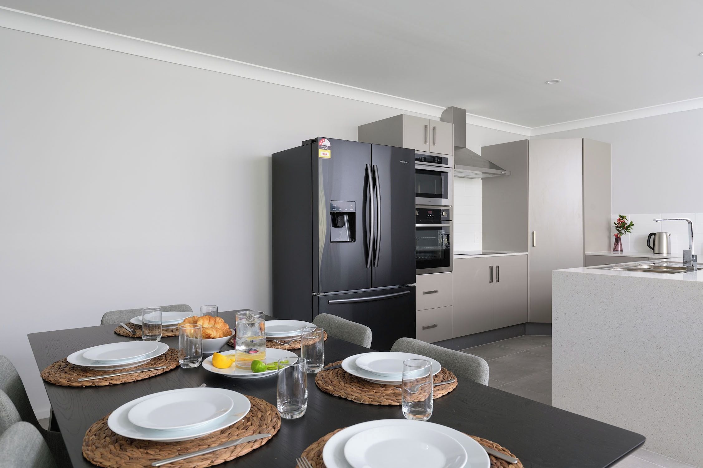 A modern kitchen with a black refrigerator, a built-in oven, and a stainless steel range hood.
