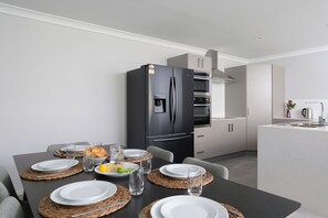 Une cuisine moderne avec un réfrigérateur noir, un four encastré et une hotte de cuisine en acier inoxydable.