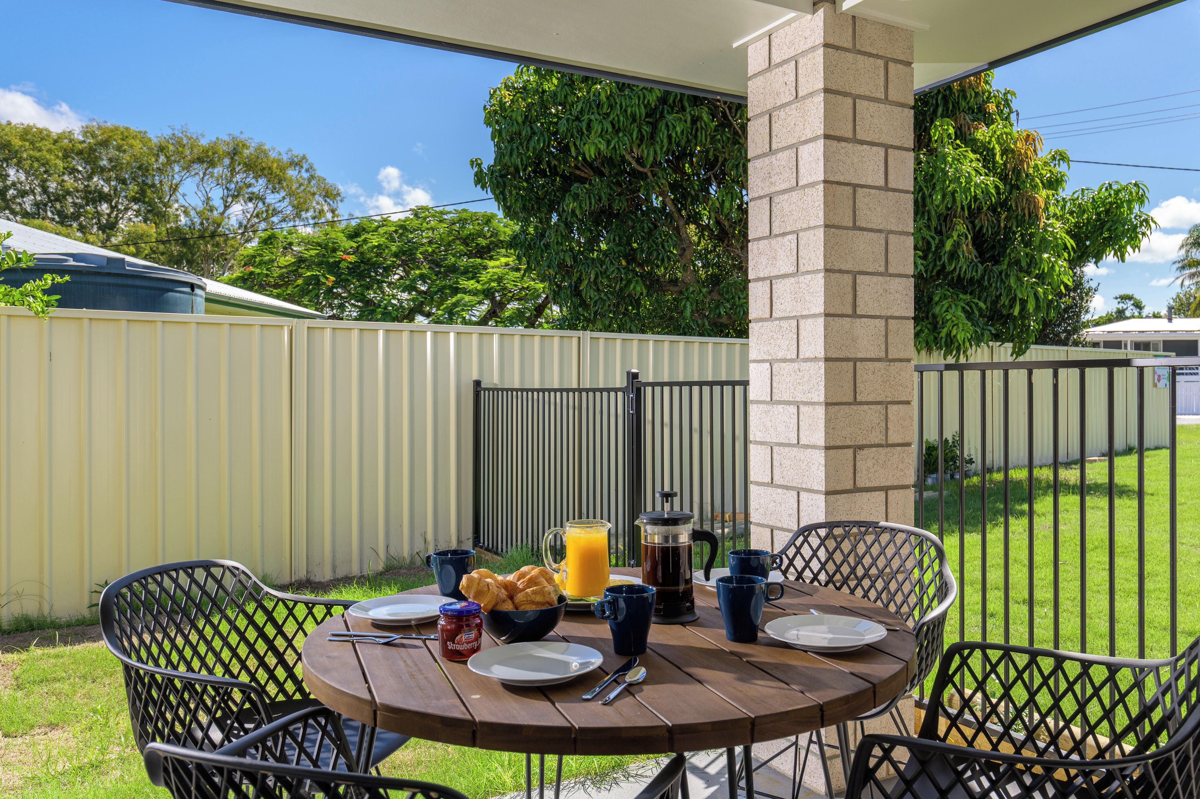 Une terrasse extérieure avec une table ronde mise pour le petit-déjeuner, comprenant des croissants, une cafetière et un verre de jus d’orange.