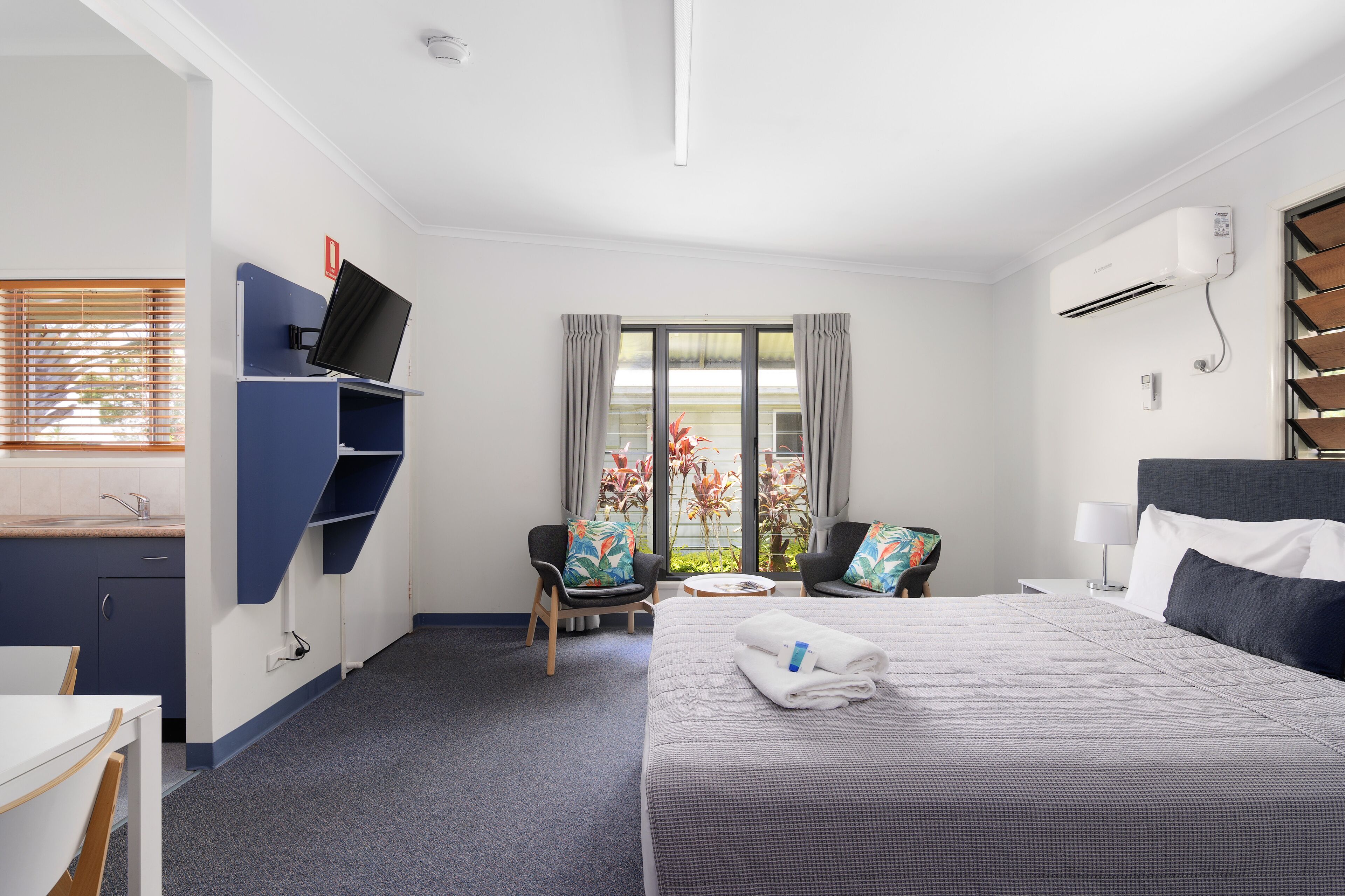 A hotel room with a bed, a desk, a chair, a TV, and a window with curtains.