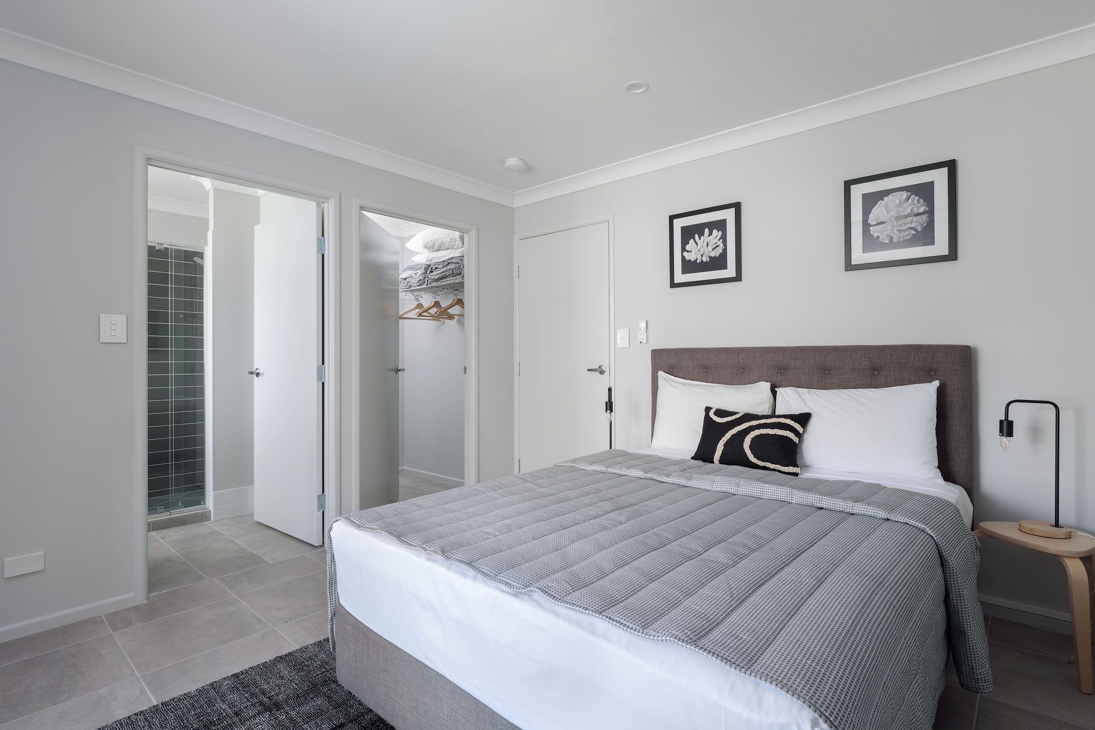 A modern bedroom with a large bed, a bedside table, a floor lamp, and two framed pictures on the wall.
