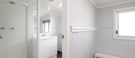 A modern bathroom with a glass shower enclosure, a white vanity, and a bench.