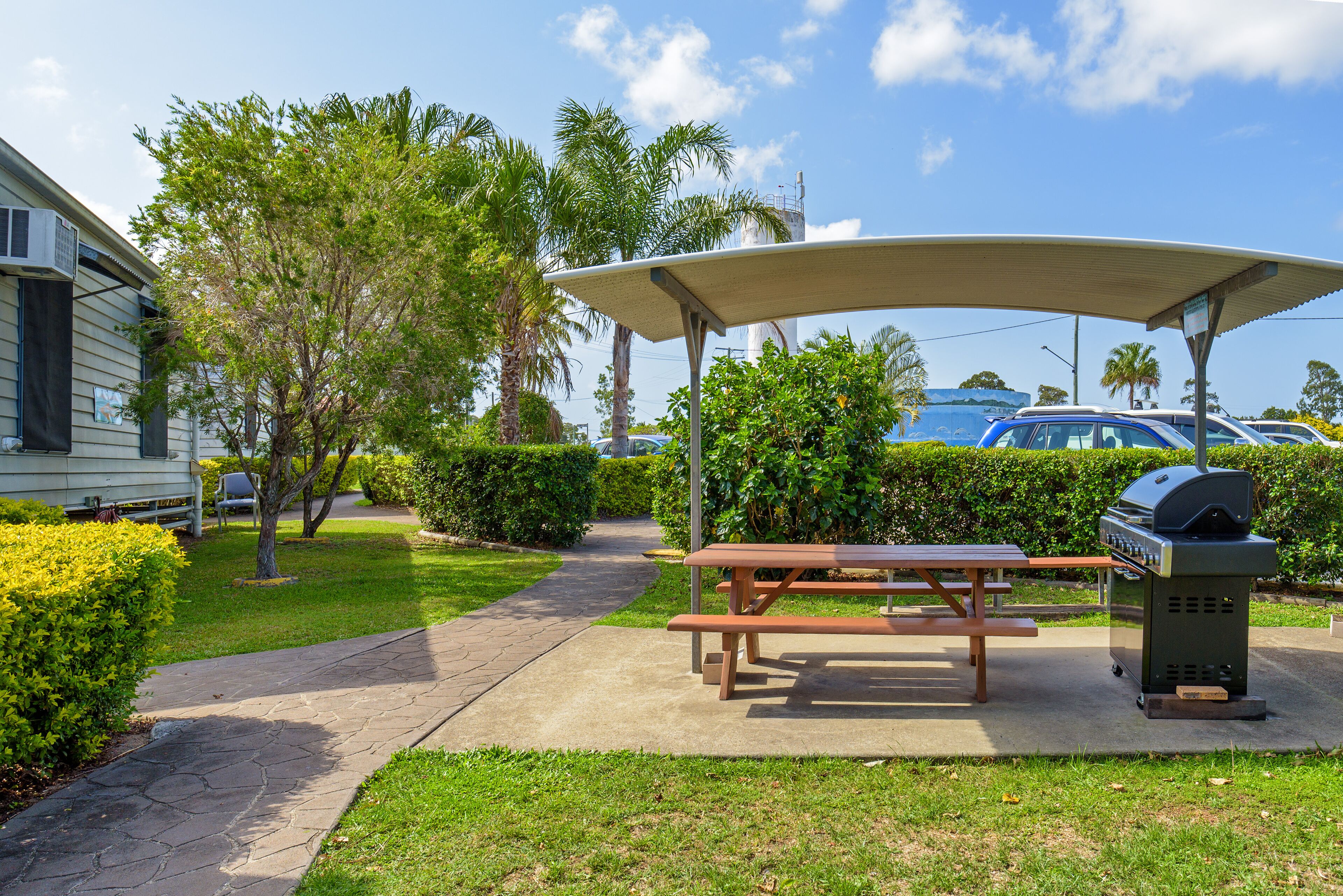 A covered picnic area with a grill, benches, and a paved walkway.