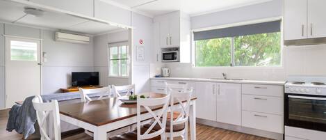 A modern kitchen with white cabinets, a wooden dining table, and a large window.