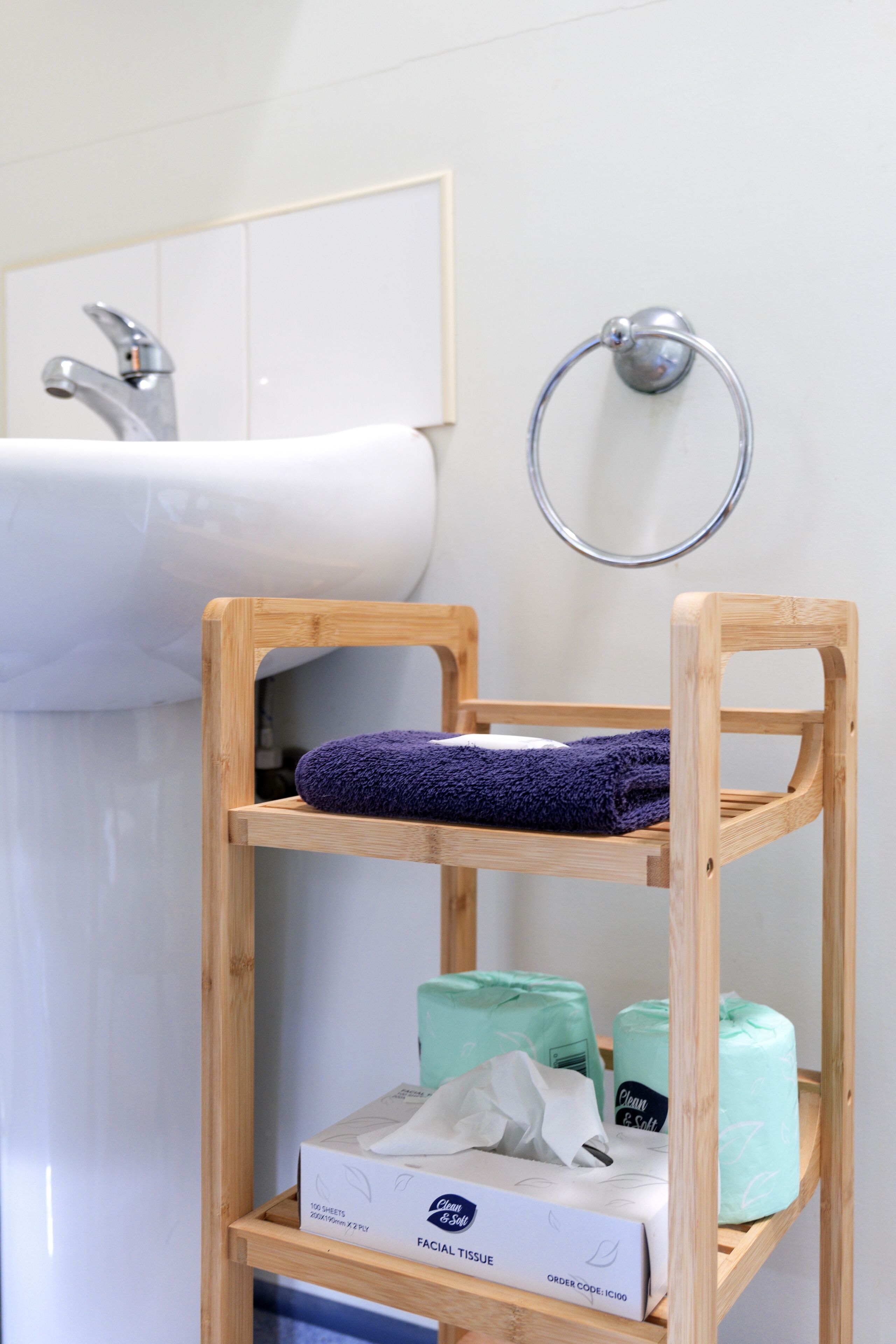 Un baño con un estante de madera que sostiene una toalla morada, pañuelos faciales y una caja de pañuelos.