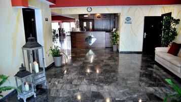 Un vestíbulo de hotel con mostrador de recepción, un sofá y plantas en macetas.
