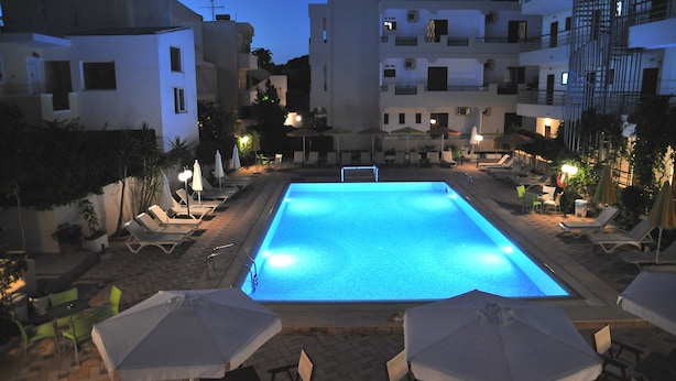 A swimming pool with lounge chairs and umbrellas, surrounded by buildings with balconies and outdoor seating. - Santa Marina Hotel Apartments (Kos)