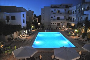 A swimming pool with lounge chairs and umbrellas, surrounded by buildings with balconies and outdoor seating. - Santa Marina Hotel Apartments (Kos)