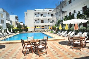 A swimming pool with sun loungers and umbrellas, surrounded by buildings. - Santa Marina Hotel Apartments (Kos)