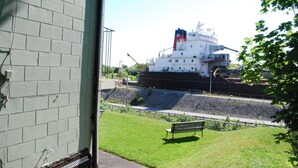 A large cargo ship docked at a port with a grassy area and a bench in the foreground.