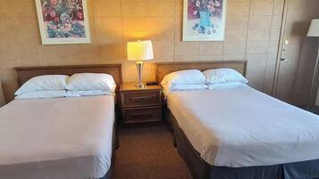 Una habitación de hotel con dos camas individuales, una mesita de noche con lámpara y dos cuadros enmarcados con motivos florales en la pared.