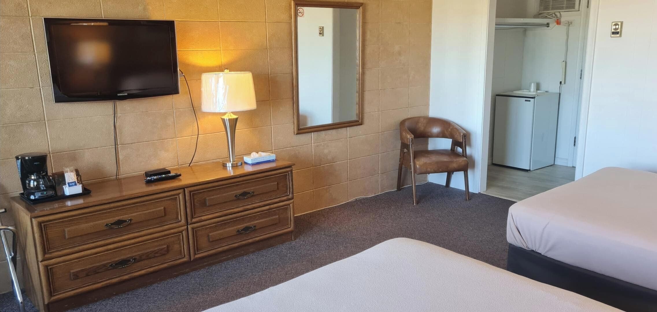 A hotel room with a TV, a lamp, a chair, a dresser, and two beds.