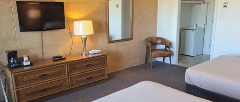 A hotel room with a TV, a lamp, a chair, a dresser, and two beds.