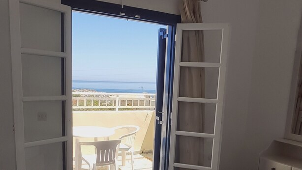 Een hotelkamer met een bed, een kledingkast, een bureau en uitzicht op zee door een open deur.