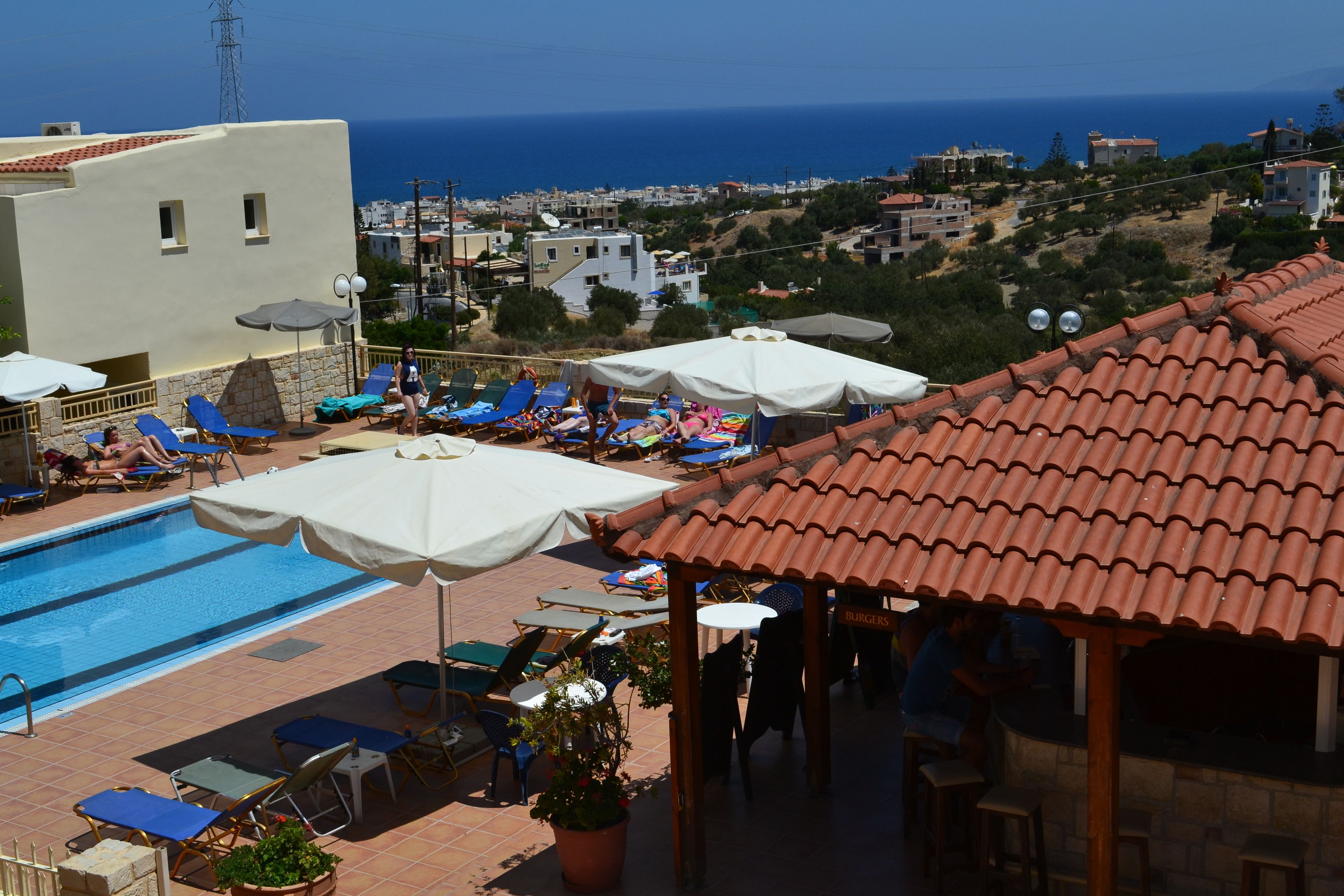 A rooftop pool area with lounge chairs and umbrellas, overlooking a coastal town.
