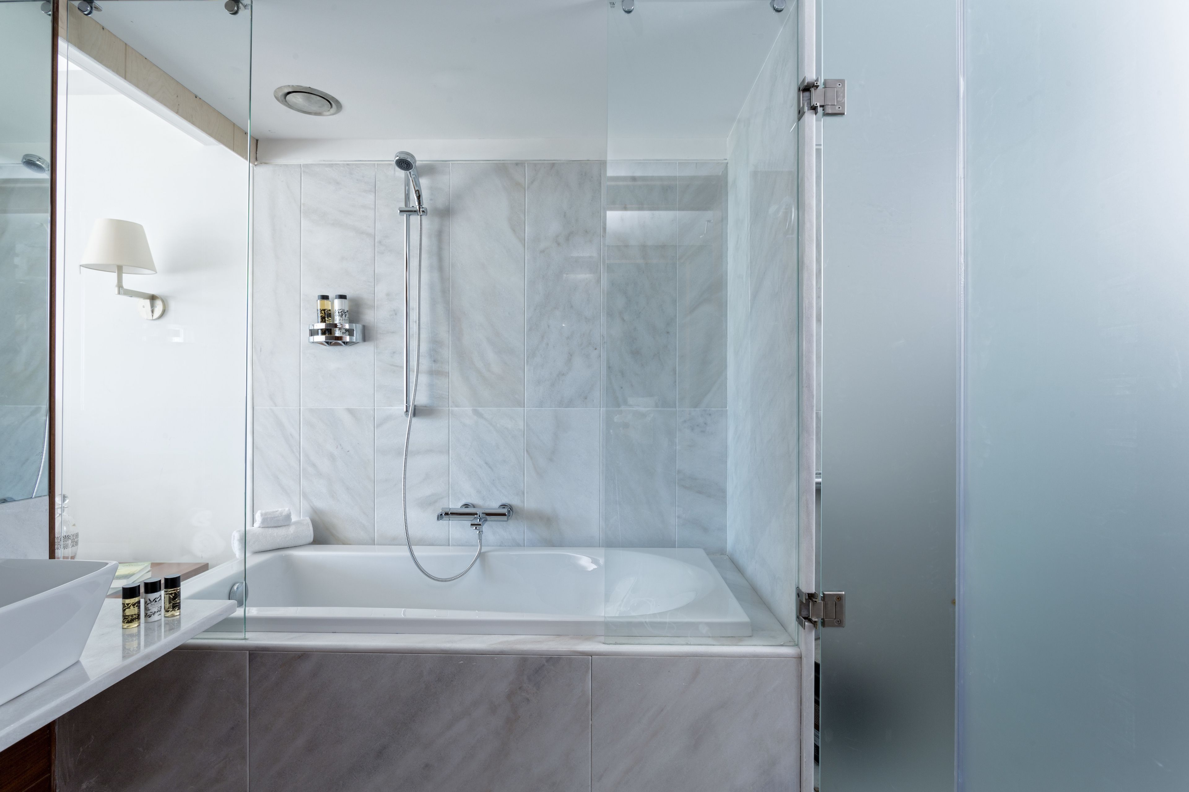 A modern bathroom with a glass-enclosed shower, a white bathtub, and a marble-tiled wall.